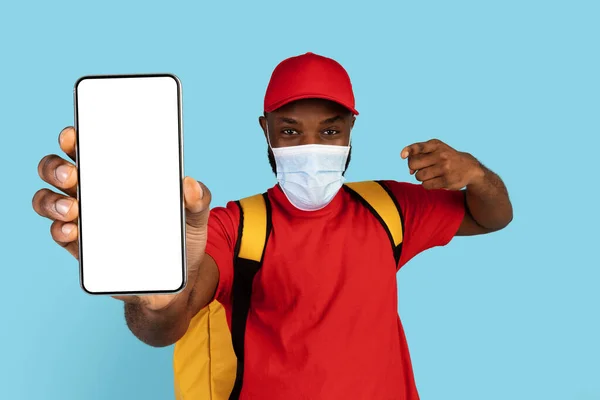 Beställ online. African American Delivery Guy In Medical Mask Demonstrerar Blank Smartphone — Stockfoto