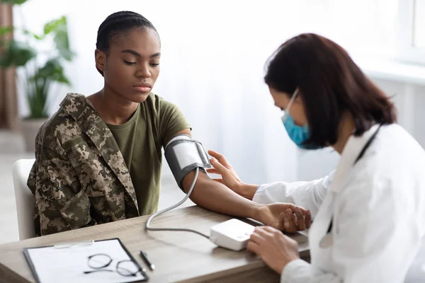 Soldat noir dame assise à la table tandis que le médecin vérifie sa tension artérielle — Photo