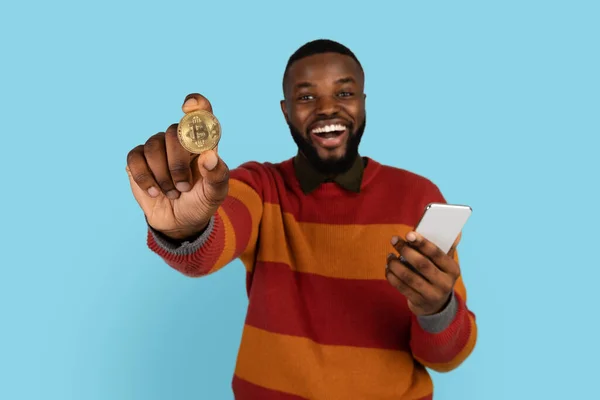 网上交易。兴奋的黑人年轻人拿着金比特币和智能手机 — 图库照片