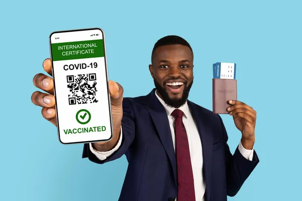 Empresario negro con pasaportes y entradas que muestra Smartphone con certificado inmunológico Covid-19 — Foto de Stock