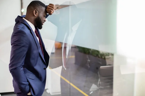 Hombre de negocios negro agotado apoyado en vidrio de ventana — Foto de Stock