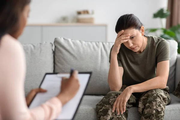 Conceito de psiquiatria militar. Deprimida senhora soldado sentado no sofá durante a sessão de terapia — Fotografia de Stock