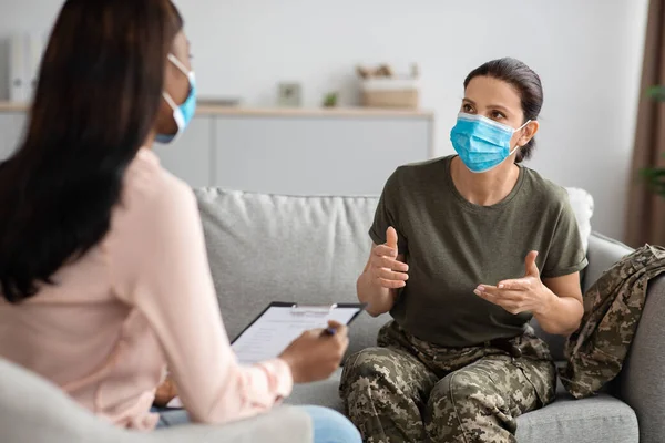 Soldado femenino con uniforme y máscara hablando con psiquiatra en la sesión de terapia —  Fotos de Stock