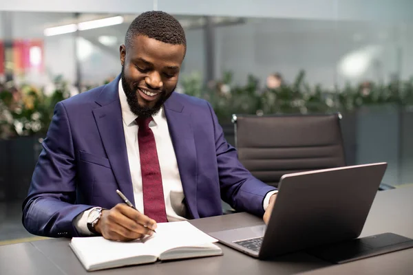 Empresário americano africano feliz usando laptop e tomando notas — Fotografia de Stock