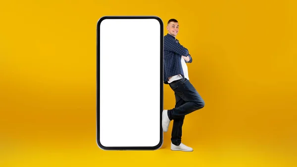 ( 영어 ) Guy Leinding On Big Smartphone With Blank Screen, Yellow Background — 스톡 사진