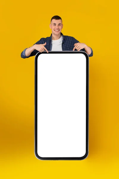 Hombre señalando en el teléfono celular grande con pantalla en blanco, fondo amarillo —  Fotos de Stock