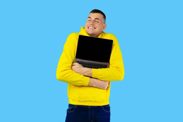 Glad kille kramar laptop med tom skärm över blå bakgrund — Stockfoto
