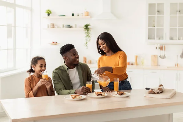 Familia negra almorzando bebiendo jugo de naranja fresco en la cocina — Foto de Stock