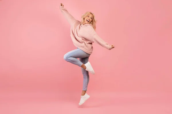 Радостная юная леди прыгает, веселится и улыбается, находясь в хорошем настроении и дурачится на розовом фоне — стоковое фото