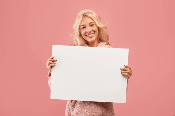 Mujer alegre mostrando un cartel publicitario vacío, sosteniendo un tablero en blanco para texto o diseño de anuncios, fondo rosa, espacio libre —  Fotos de Stock