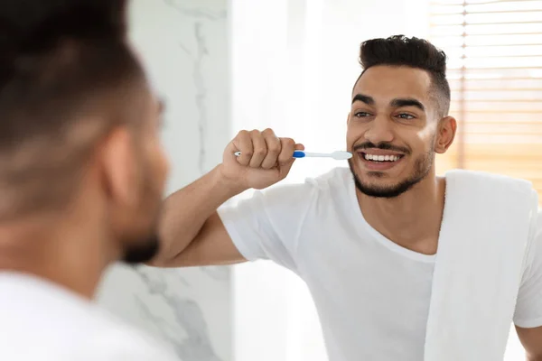 Guapo milenario árabe chico cepillándose los dientes con cepillo de dientes en el baño, — Foto de Stock