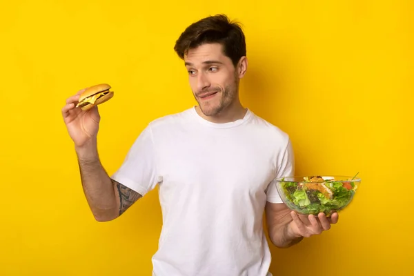 Retrato de tipo divertido sosteniendo hamburguesa y ensalada —  Fotos de Stock