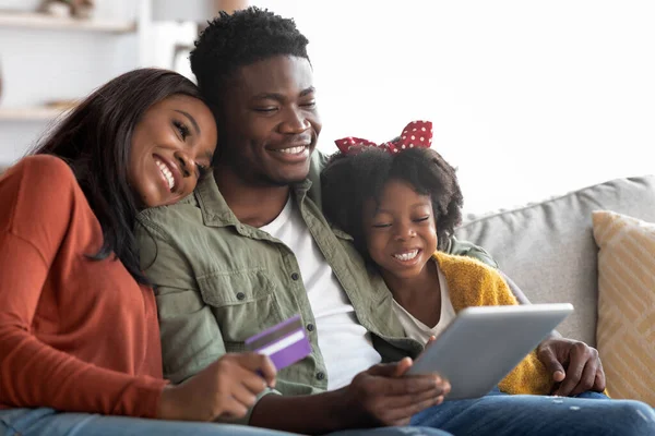 Концепция электронной коммерции. Улыбка афроамериканской семьи с помощью цифрового планшета и кредитной карты — стоковое фото
