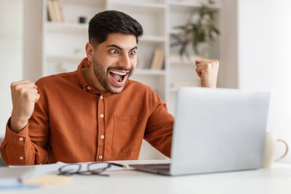 Uomo arabo utilizzando il computer portatile che celebra il successo scuotendo pugni urlando sì — Foto Stock