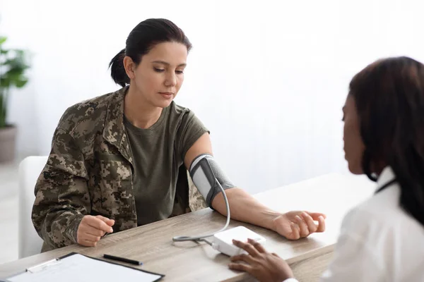 Fekete orvos nő méri a vérnyomást a hölgy katonai egyenruhában — Stock Fotó