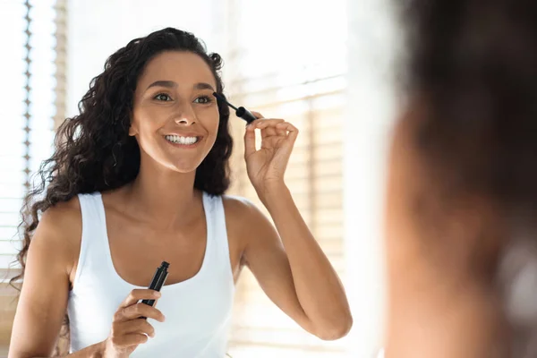 Concepto de maquillaje. Atractiva hembra feliz aplicación de máscara en las pestañas cerca del espejo — Foto de Stock