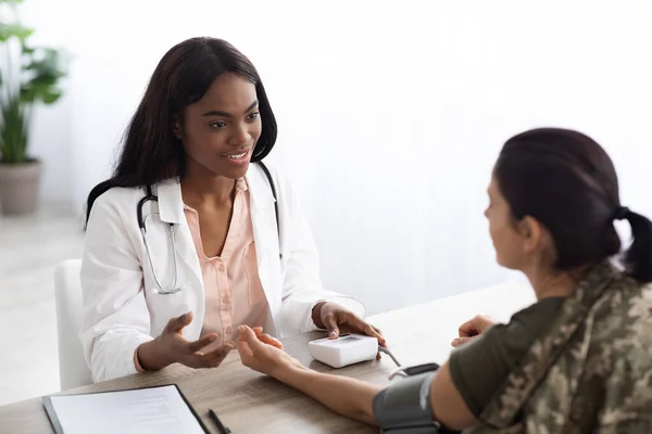 Médico negro mujer consultando soldado femenino y comprobando su presión arterial —  Fotos de Stock