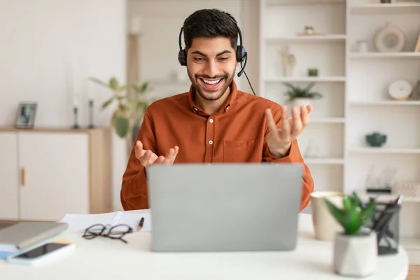 Arab za pomocą laptopa w słuchawkach siedzi przy biurku — Zdjęcie stockowe
