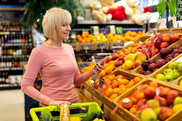 スーパーで買い物をしながら携帯電話を使うシニア女性 — ストック写真