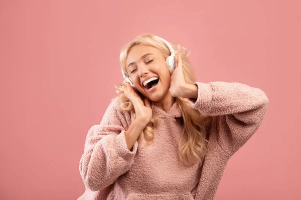 Los auriculares estéreo más nuevos. Emocionada dama disfrutando de la lista de reproducción con los ojos cerrados en los auriculares inalámbricos, fondo rosa — Foto de Stock