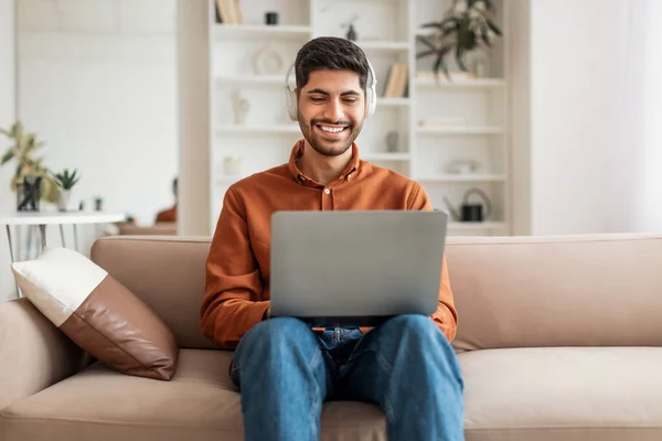 Hombre árabe sonriente usando PC en casa, escuchando música — Foto de Stock