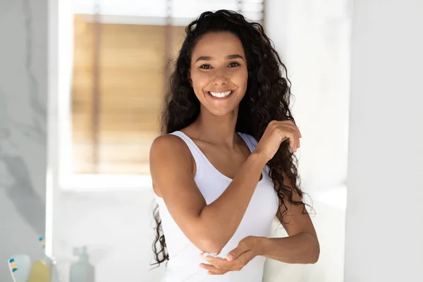 Mooie jonge vrouw plassen vochtinbrengende crème op de elleboog terwijl staande in de badkamer — Stockfoto