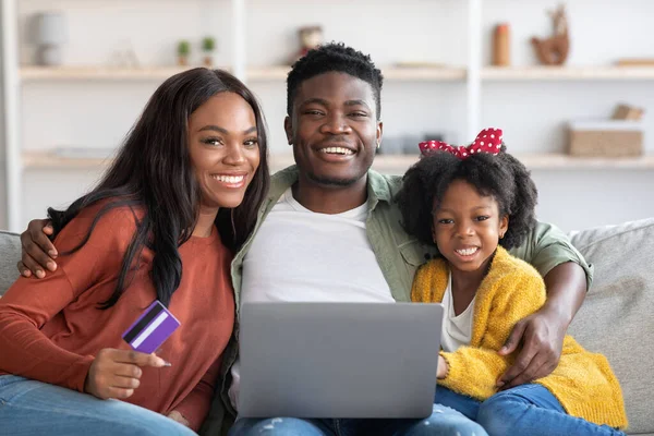 Bokningar online. Porträtt av lycklig svart familj med bärbar dator och kreditkort — Stockfoto