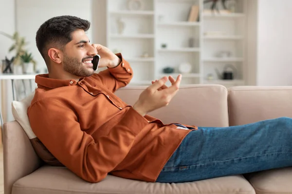 Glada arabiska man talar på mobiltelefon liggande på soffan — Stockfoto