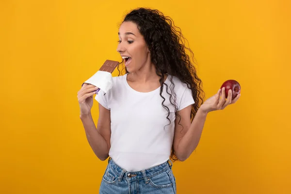 Porträtt av upphetsad dam håller Apple och bita choklad — Stockfoto