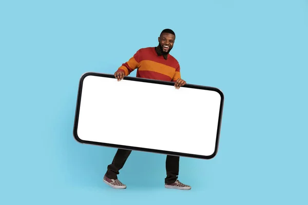 Mobilní reklama. Šťastný mladý černošky muž nesoucí velký prázdný smartphone — Stock fotografie