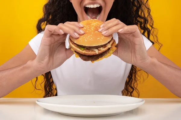 Closeup de senhora segurando hambúrguer mordendo sanduíche no estúdio — Fotografia de Stock
