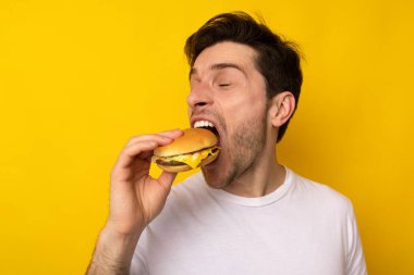 Stüdyoda Burger Isıran Komik Aç Adam sandviç tutuyor.