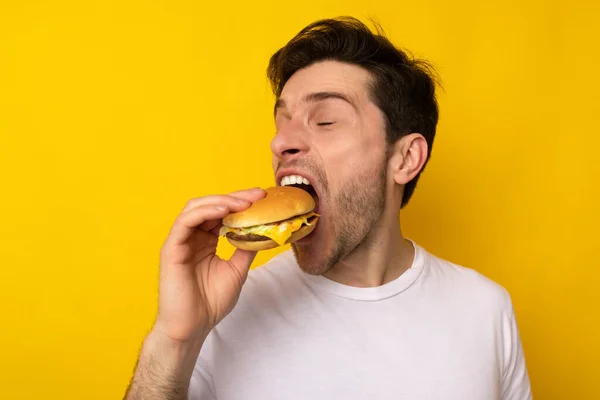 Engraçado fome cara segurando hambúrguer mordendo sanduíche no estúdio — Fotografia de Stock