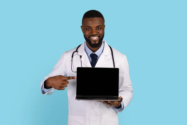 Beyaz cüppeli yakışıklı siyah doktor boş laptop ekranını işaret ediyor. — Stok fotoğraf