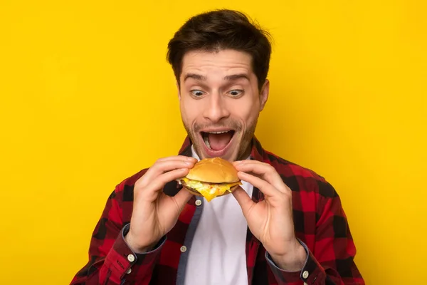Emocionado divertido joven sosteniendo hamburguesa en el estudio — Foto de Stock