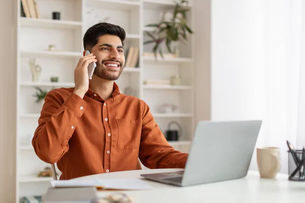 Uśmiechnięty brodaty mężczyzna pracujący i rozmawiający przez telefon w domu — Zdjęcie stockowe