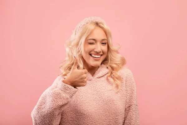 Ganska snygg dam visar tummen upp, blinkar och ler mot kameran, rekommendera något, rosa bakgrund — Stockfoto