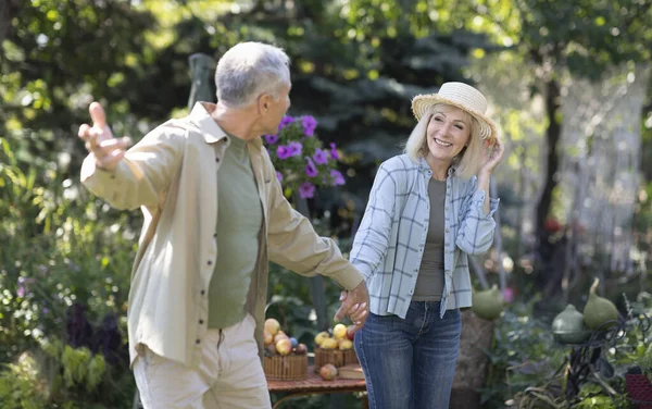 Счастливая любящая пожилая пара, держась за руки и гуляя в своем саду в теплый весенний день, наслаждаясь временем вместе — стоковое фото