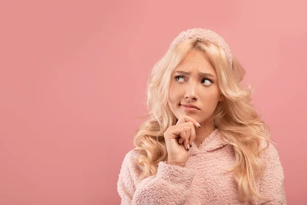 Een keuze maken. Pensive jonge dame aanraken kin en opzij te kijken naar de vrije ruimte, denken aan iets, roze achtergrond — Stockfoto