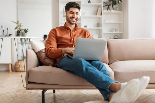 Uśmiechnięty Arab korzystający z komputera w domu, słuchający muzyki — Zdjęcie stockowe