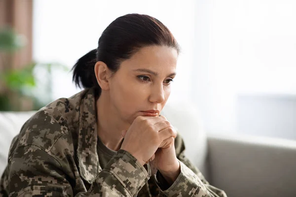 Mujer soldado pensativa con estrés postraumático sentada en el sofá y mirando hacia otro lado — Foto de Stock