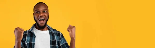 Podekscytowany czarny facet trzęsące się pięści pozowanie na żółtym tle, Panorama — Zdjęcie stockowe