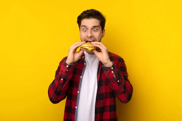 Divertido tipo hambriento sosteniendo hamburguesa mordiendo sándwich en el estudio — Foto de Stock