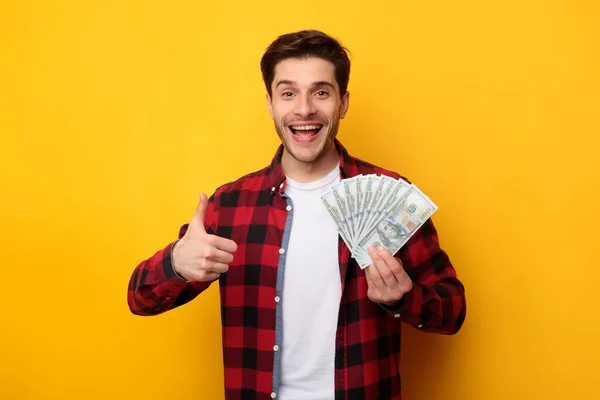 Hombre excitado sosteniendo dinero en efectivo y pulgares hacia arriba —  Fotos de Stock