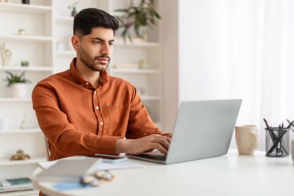 Homem árabe usando laptop sentado na mesa no escritório — Fotografia de Stock