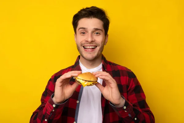 Sorrindo jovem cara segurando hambúrguer no estúdio — Fotografia de Stock