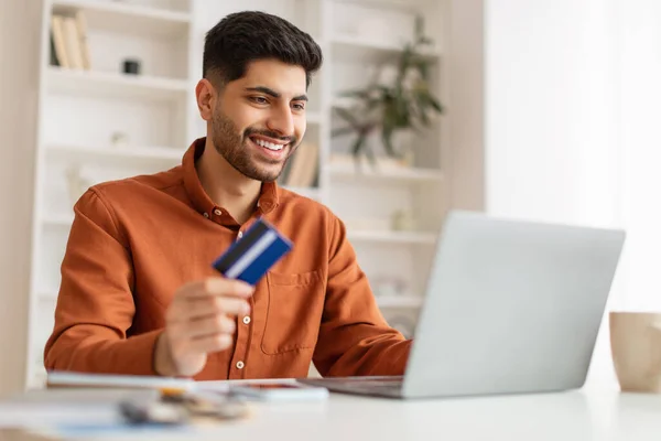 Smiling young man using pc and credit card at home — Stock Photo, Image