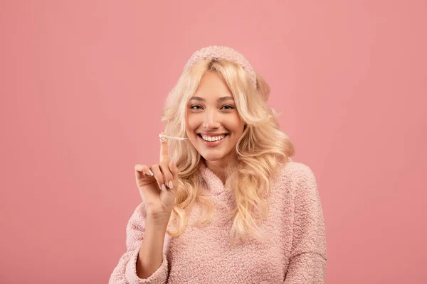 Glad ung kvinna sträcker tuggummi från munnen och ler mot kameran, rosa studio bakgrund — Stockfoto
