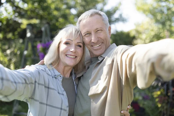 Felices cónyuges mayores haciendo selfies, abrazando, sonriendo a la cámara, pasando tiempo juntos en su jardín al aire libre —  Fotos de Stock
