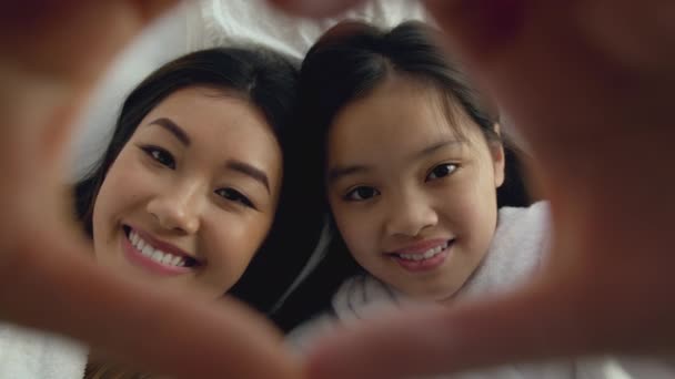 Top ver retrato de feliz asiático madre e hija sonriendo a cámara a través de corazón gesto marco — Vídeos de Stock